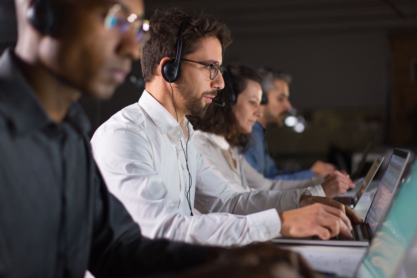 Customer service agents wearing headsets and working at laptops in a shared office