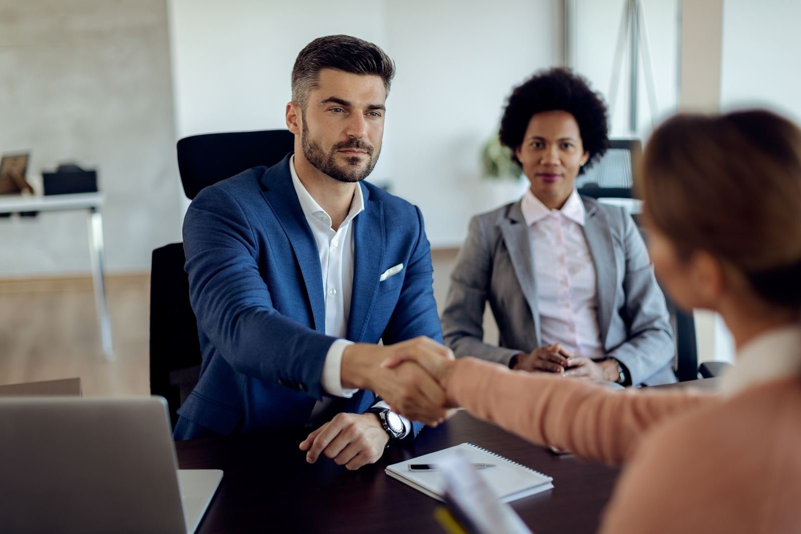 Two people shaking hands with a third across a meeting table